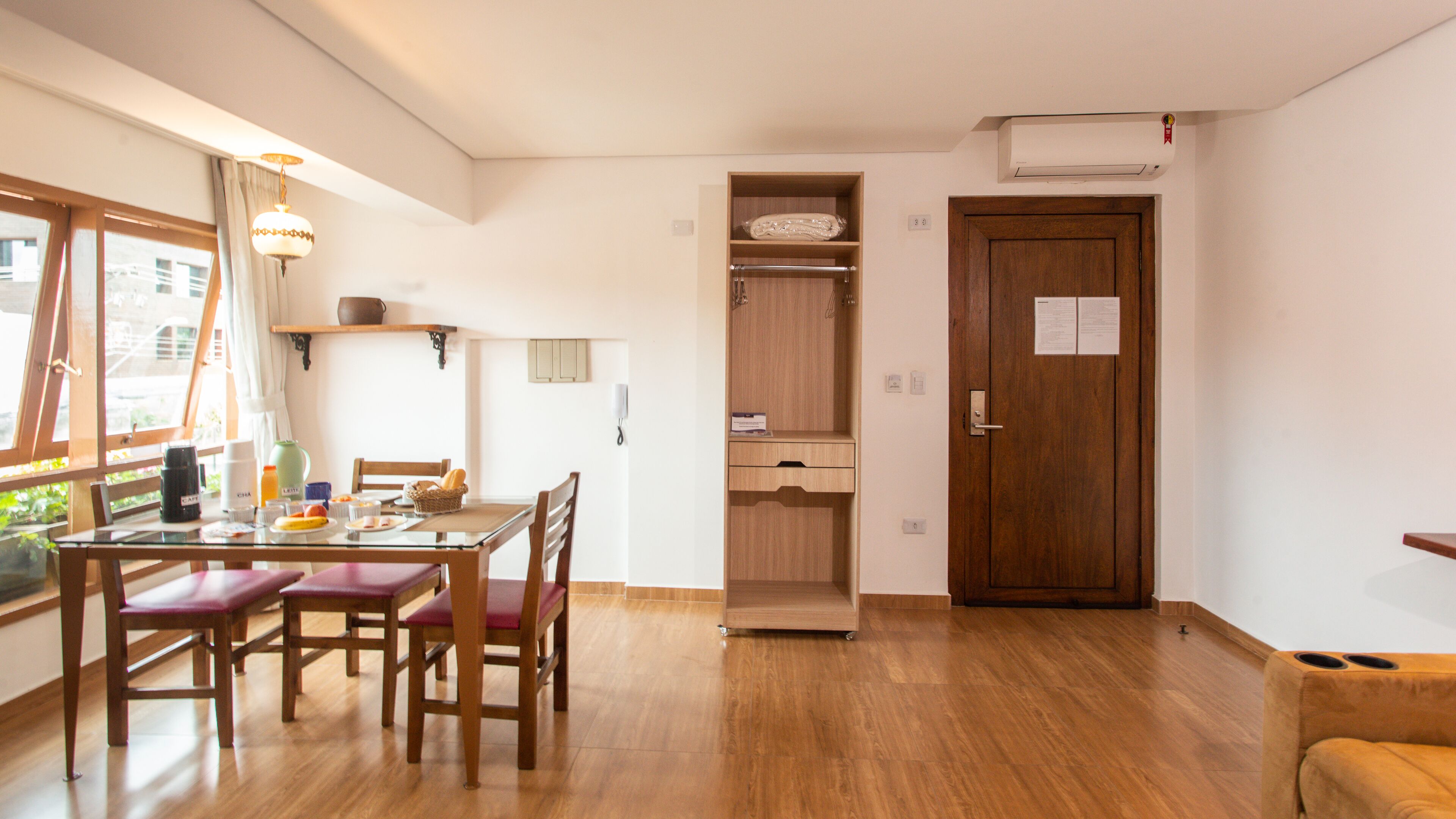 A dining area with a wooden table and chairs, a window with curtains, and a wooden wardrobe with a door.