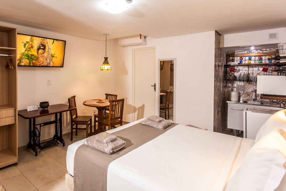 Quarto de hotel com cama, secretária, cadeira, guarda-roupa e cozinha.