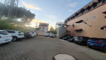 A parking lot with multiple cars, a brick building with a staircase, and a tall metal structure in the background.