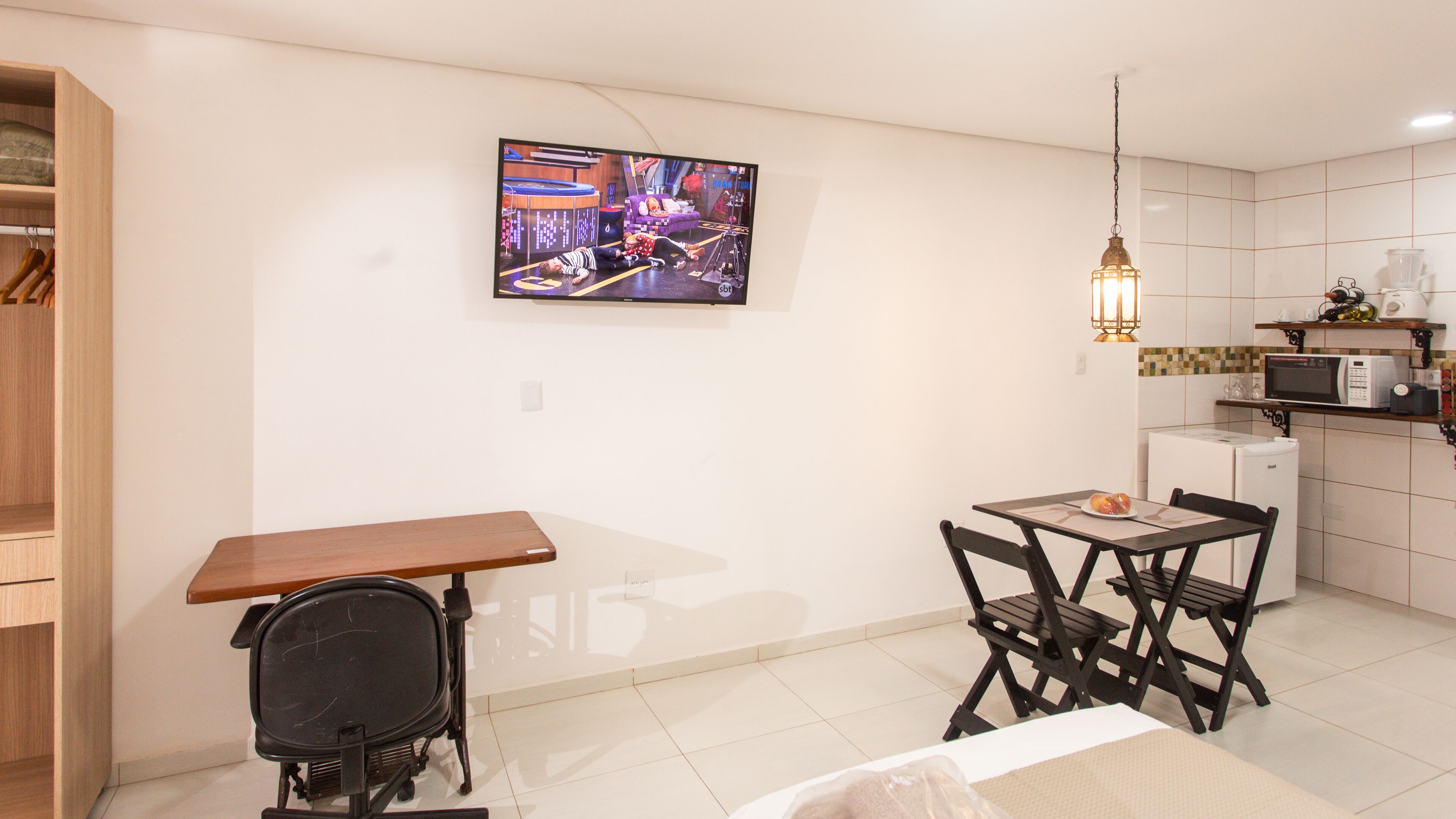 Un espace de vie compact comprenant un coin repas, une kitchenette et un téléviseur fixé au mur.