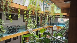 Un atrio de varios niveles con plantas colgantes, barandillas de vidrio y una zona de piscina.