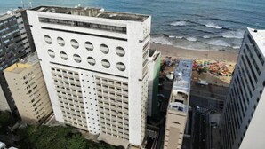 Een hoog gebouw met een opvallend cirkelvormig raam patroon, naast een strand met kleurrijke parasols.