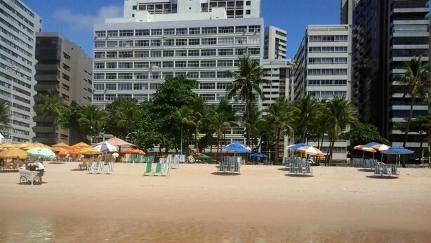Een strand met parasols en stoelen, palmbomen en hoge gebouwen op de achtergrond.