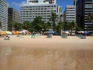 Una playa con sombrillas y sillas, palmeras y edificios altos al fondo.