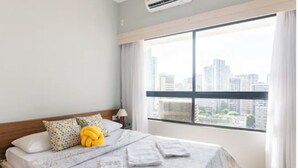 Een hotelkamer met een groot raam, een bed met een bedovertrek met dessin en uitzicht op de stad.