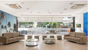 Een moderne lobby met beige banken, glazen salontafels en grote ramen met uitzicht op de straat en palmbomen.