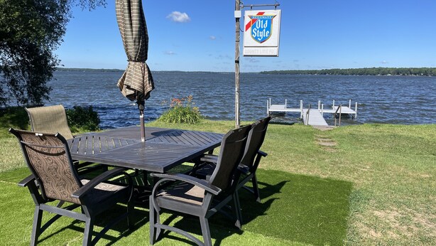 Een terras aan het water met een tafel, stoelen en een parasol, en een bordje voor 'Old Style' bier.