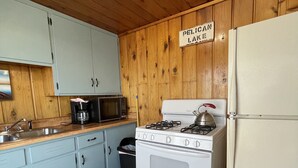 Een keuken met houten wanden, een fornuis, een koelkast en een spoelbak.