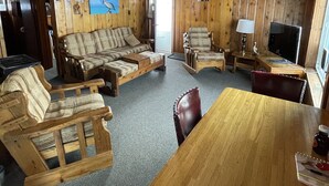 Een houten chalet van binnen met een zithoek, een eettafel en een televisie.