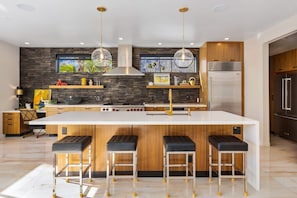 A modern kitchen with a central island, bar stools, wooden cabinetry, stainless steel appliances, and pendant lighting.