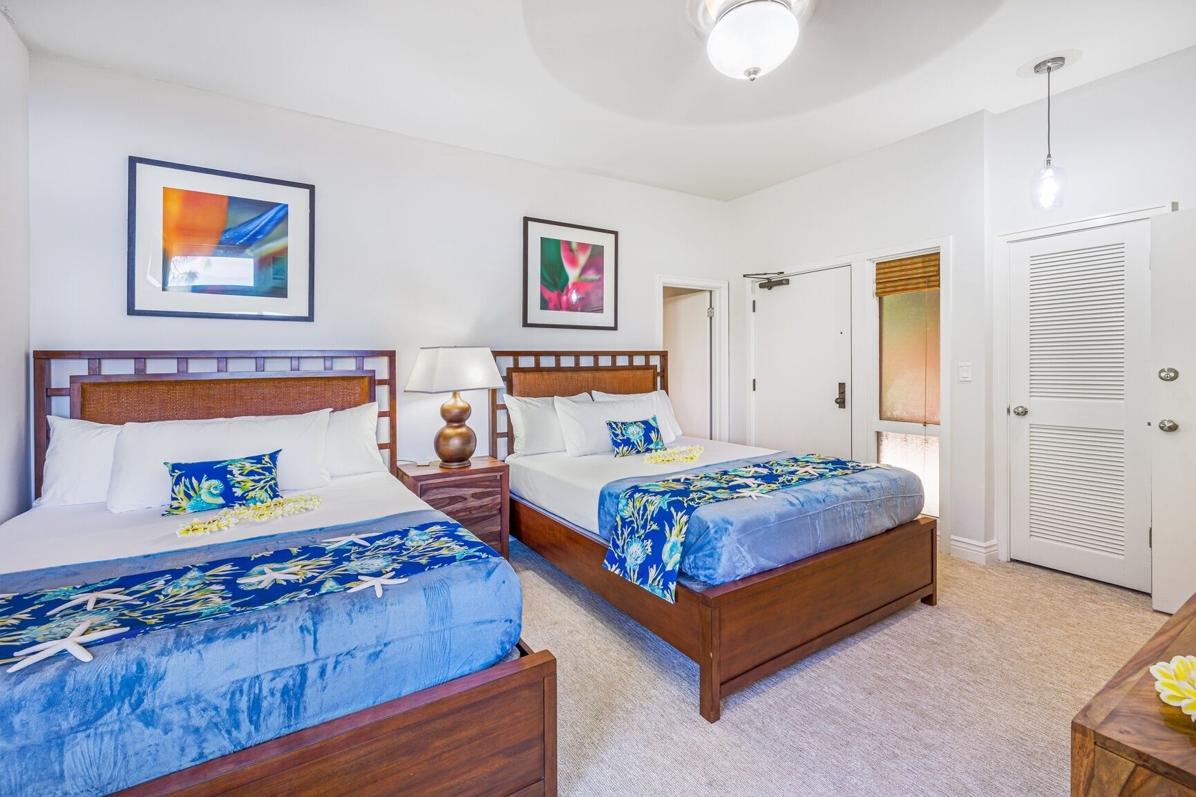 A hotel room with two beds, a nightstand, a lamp, and a door with a mirror.