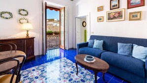 A living room with a blue sofa, a wooden coffee table, a desk with a lamp, and a patterned floor. - Stefania Flat- Amalfi centre (Amalfi)