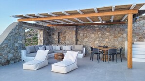 Un espace extérieur aménagé avec des murs en pierre, doté d’une pergola en bois, d’un canapé et d’une table à manger avec des chaises.