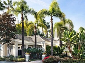 A residential building with a symmetrical facade, multiple windows, and a well-maintained garden with palm trees and shrubs. - CLOUD NINE • Comfort & Elegance <br>Penthouse Condo (Irvine)