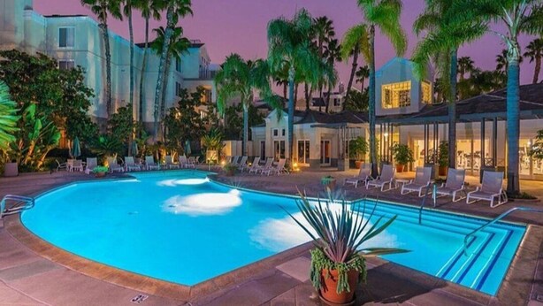 Ein Pool mit Liegestühlen und Palmen, umgeben von Gebäuden.