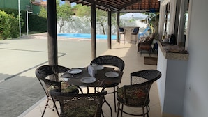 En uteplats med ett takförsett sittområde, ett bord för två och utsikt över en swimmingpool.