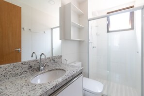 A bathroom with a granite countertop sink, a white toilet, and a glass shower enclosure.