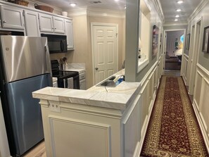 Una cocina con armarios blancos, un refrigerador de acero inoxidable, un microondas negro y una encimera de mármol.