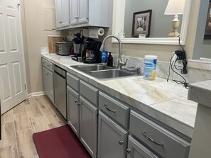 A kitchen with a marble countertop, stainless steel sink, and grey cabinets.