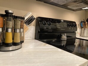 Una cocina con estufa negra, encimera de mármol y especieros.