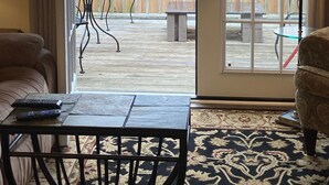 A room with a sliding glass door leading to an outdoor patio. The patio has a wooden deck, a round table, and a bench. There is a lamp on the patio, and a sofa and a small table inside the room. - Classic City 3 bed 2 bath condo with deck close to Five Points & UGA in Athens (Athens)