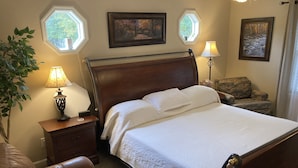 Un dormitorio ordenado con una cama de madera, una mesita de noche con una lámpara, una silla y dos cuadros enmarcados en la pared.
