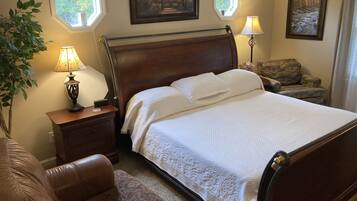 A neatly arranged bedroom with a wooden bed, a nightstand with a lamp, a chair, and two framed pictures on the wall.