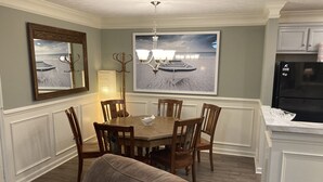 A dining area with a wooden table, six chairs, a chandelier, a large framed picture of a boat on the water, and a black refrigerator in the background. - Classic City 3 bed 2 bath condo with deck close to Five Points & UGA in Athens (Athens)