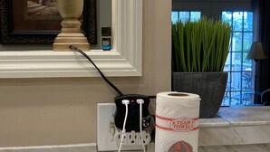 Un baño con encimera de mármol, dispensador de toallas con una toalla, una lámpara y un enchufe con cables.