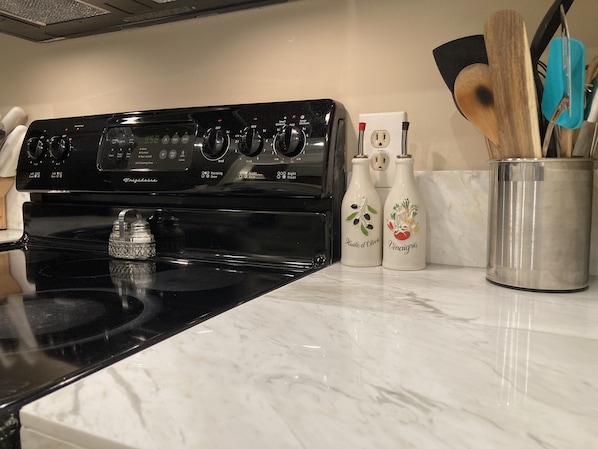Una cocina con estufa negra, encimera blanca y dos botellas de cocina con etiquetas.
