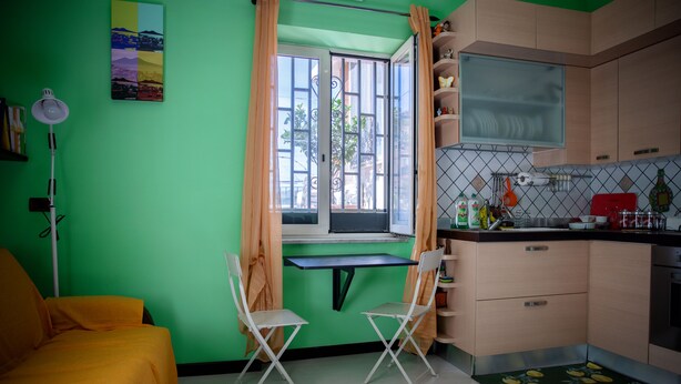 Uma cozinha compacta com área de refeições, com uma parede verde, uma pequena janela com cortinas e um sofá amarelo.