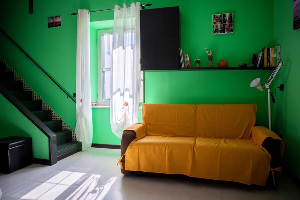 A room with a green wall, a yellow sofa, a staircase, and a window with white curtains.