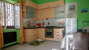 Uma cozinha com armários de madeira clara, uma geladeira de aço inoxidável e uma mesa de jantar com tampo de vidro.