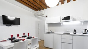Una cocina moderna con armarios blancos, un microondas, un hervidor y un televisor de pantalla plana montado en la pared.