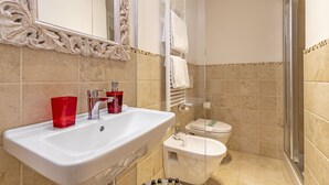 Un baño con un lavamanos blanco, vidrio rojo y un bidé.