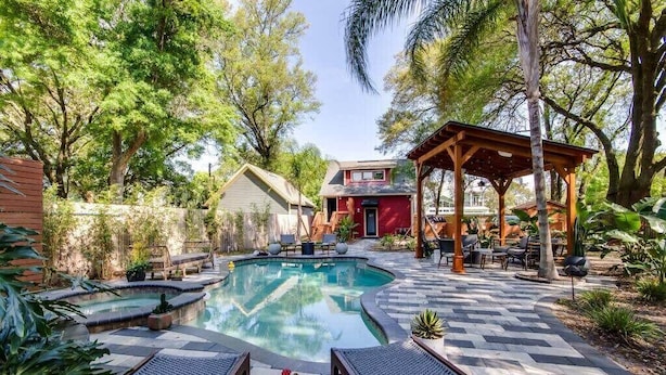 Un patio trasero con piscina, sillas de descanso, un pabellón y una casa.