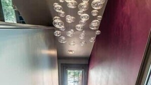 Uma escada com tapete vermelho, corrimão de metal e luminárias esféricas no teto.