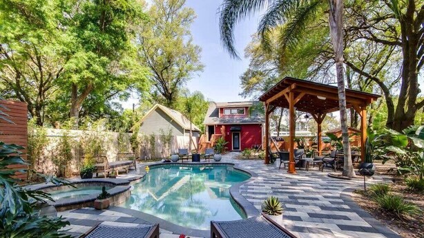 Quintal com piscina, cadeiras de descanso, um gazebo e uma casa.
