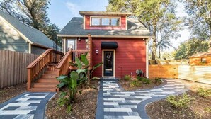 Uma casa vermelha com uma escadaria de madeira que leva à porta da frente, rodeada por um jardim com um caminho decorativo.