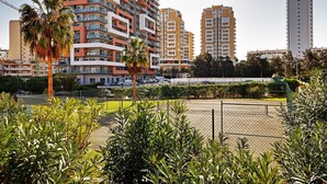 Un quartier résidentiel avec de grands immeubles, un court de tennis clôturé et des palmiers.