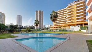 Une piscine entourée d’une terrasse carrelée, avec un grand immeuble en arrière-plan.