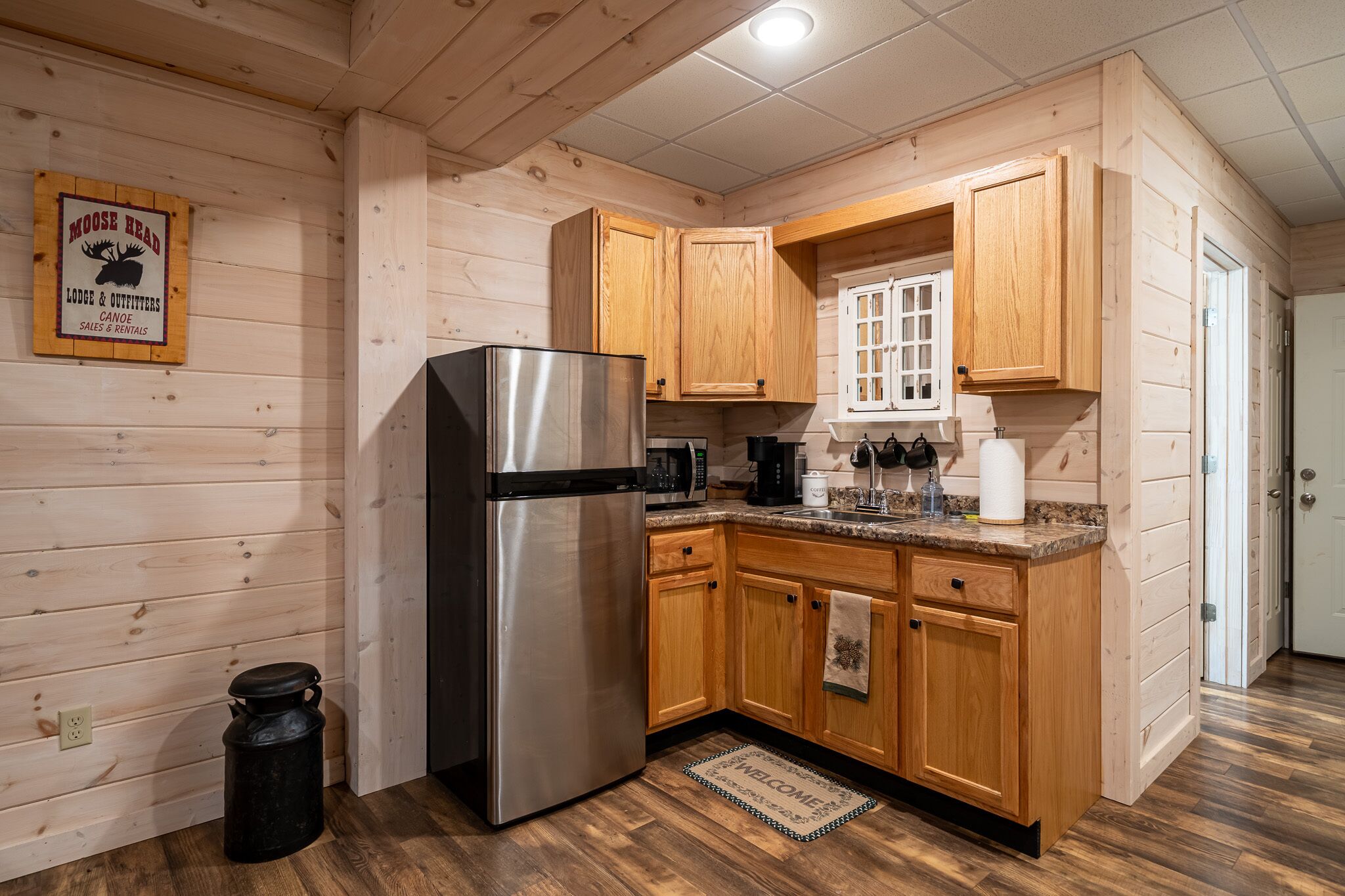 A compact kitchen with wooden cabinets, a stainless steel refrigerator, and a coffee maker.