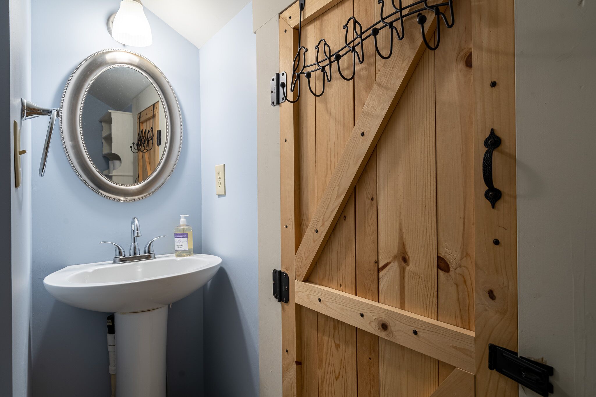 A bathroom with a white sink, a round mirror, and a wooden door with a metal handle.