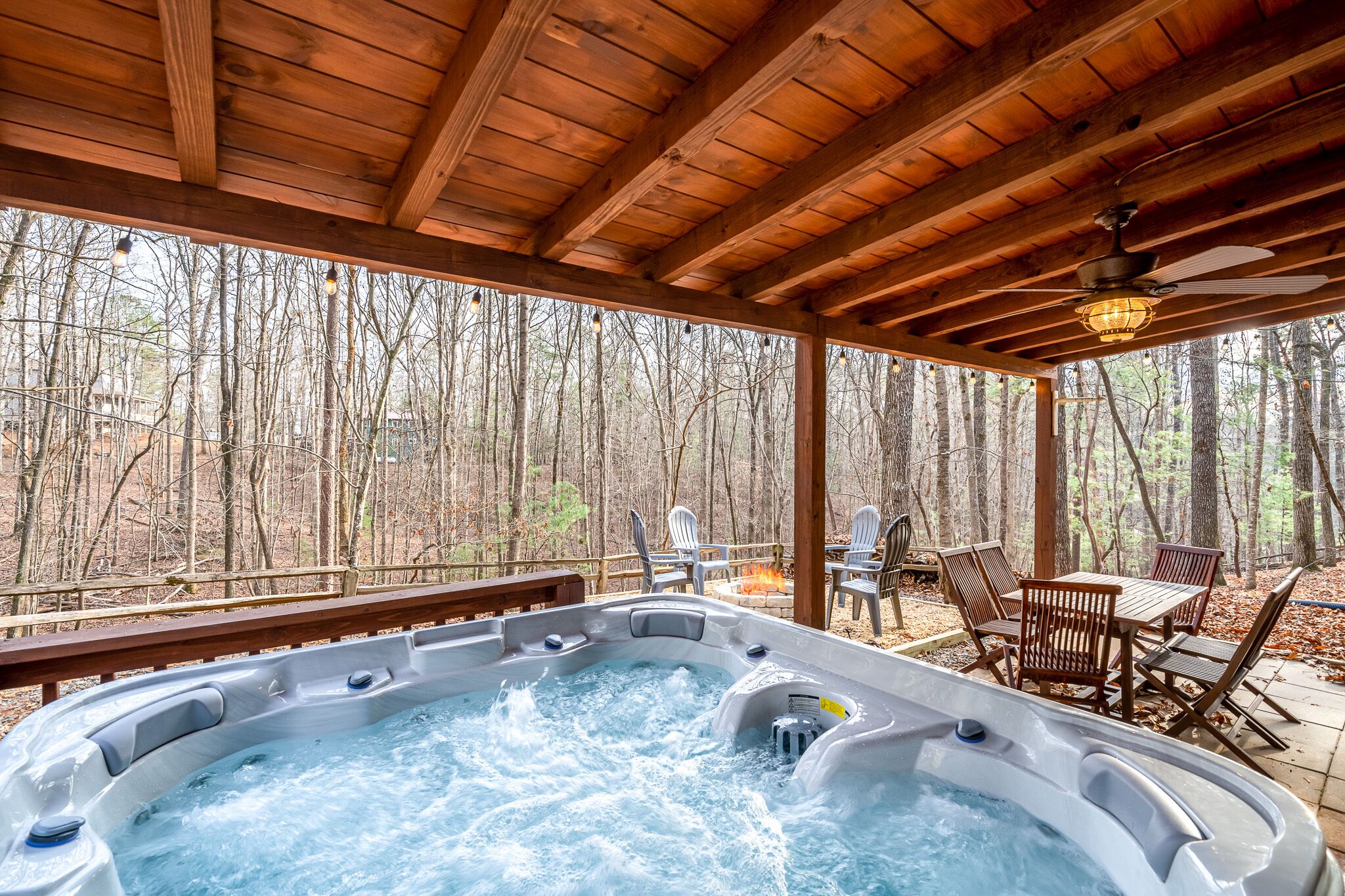 A hot tub under a wooden pergola with a forest view.