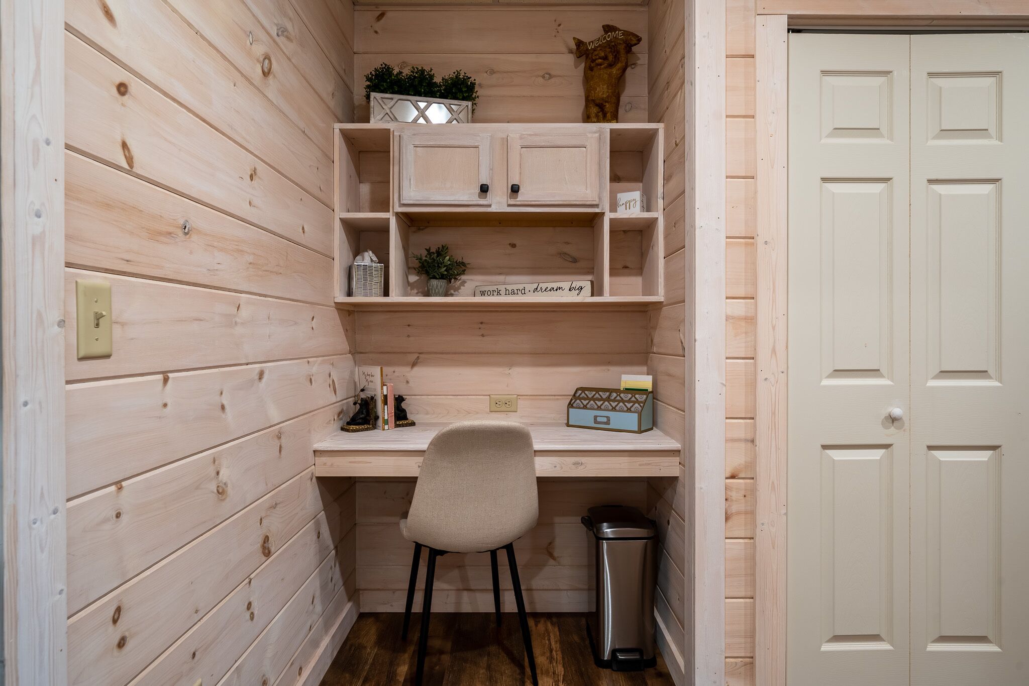 A small, wooden-paneled room with a desk, chair, and shelves.