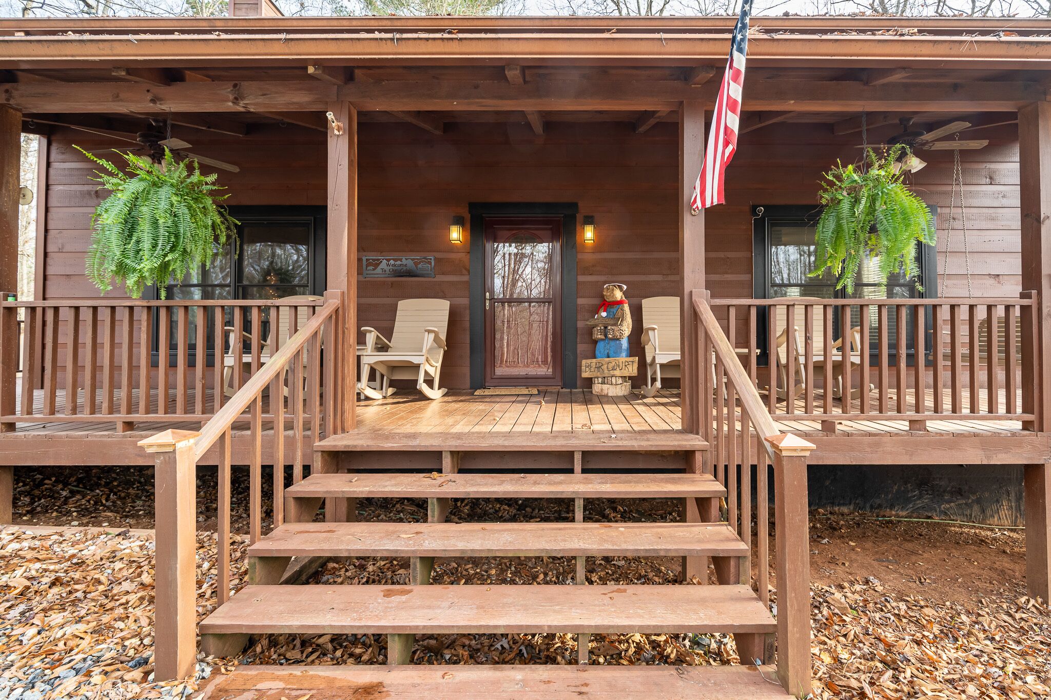 A wooden cabin with a porch, two rocking chairs, and a bear statue.