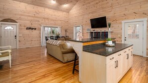 Une cuisine spacieuse aux murs en bois et dotée d’un îlot central, un salon confortable avec un canapé et une table à manger.