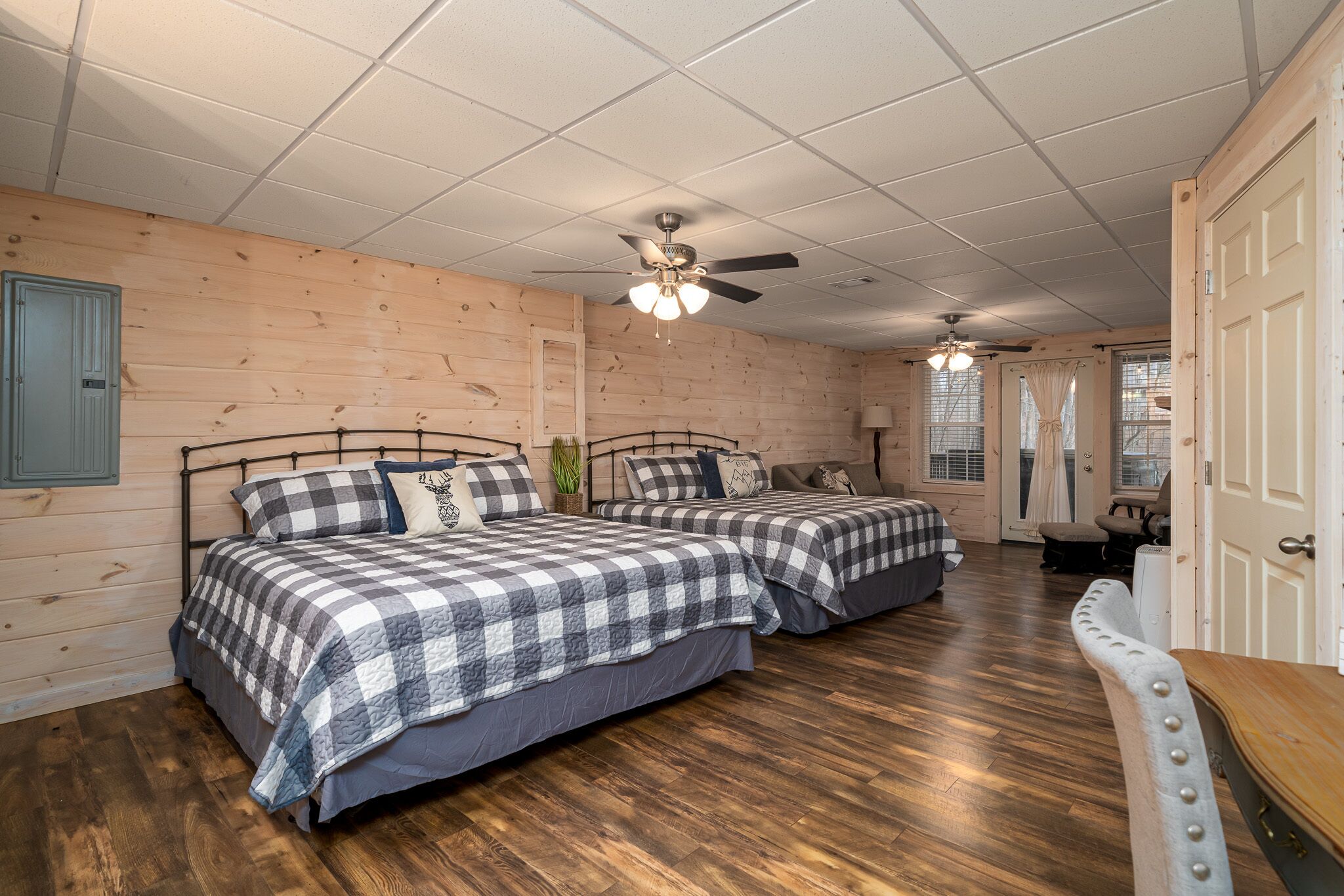 A room with two beds, wooden walls, a ceiling fan, and a door.
