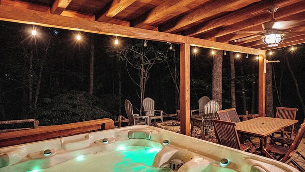 Un espace avec un jacuzzi, doté de mobilier en bois et illuminé de guirlandes lumineuses.