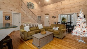 Un intérieur de chalet chaleureux avec un escalier, deux canapés, une table basse et un sapin de Noël blanc.